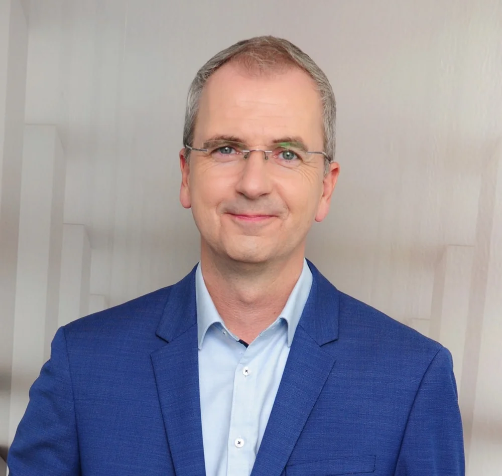 Oliver Stamm, Inhaber der Geldexperten, im blauen Sakko vor hellem Hintergrund